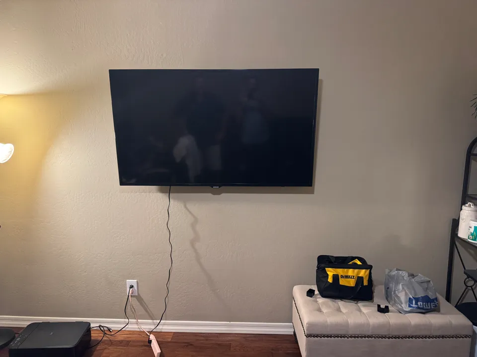 65-inch Samsung TV mounted level on the office wall, with its power cord running down to the existing outlet below