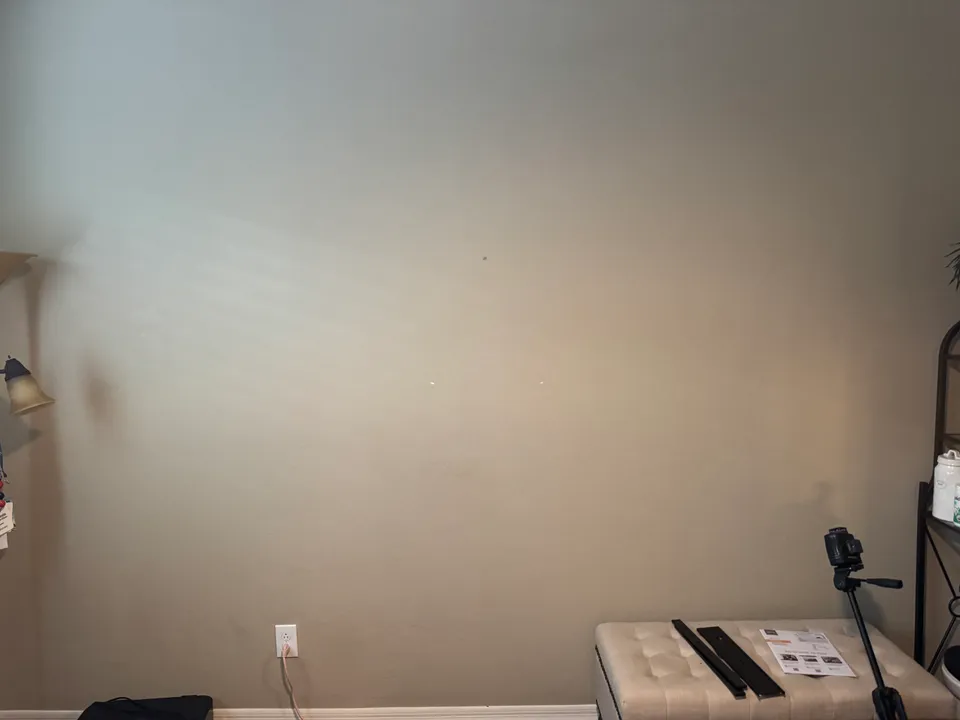 Bare office wall with laser-level marks where the mount will go, the mount rails laid out on a bench, and an outlet near the floor